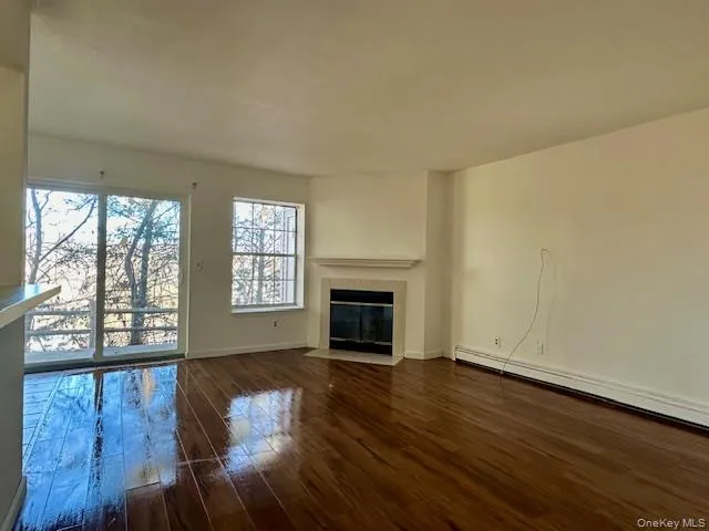 Unfurnished living room with dark wood finished floors, a fireplace, and a baseboard heating unit Unfurnished living room with dark wood finished floors, a fireplace, and a baseboard heating unit