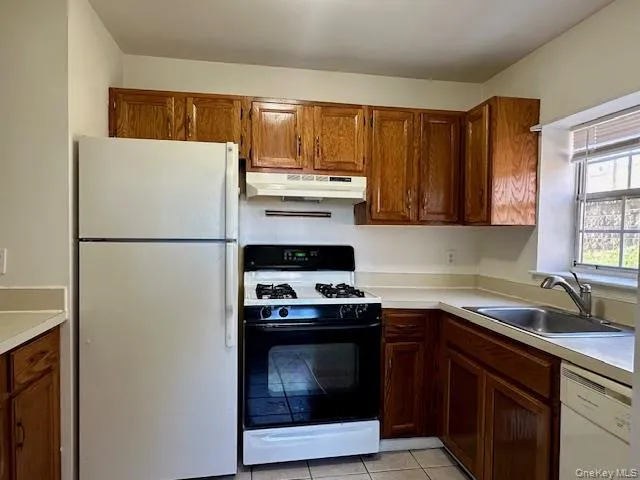 Kitchen featuring white appliances, light countertops, brown cabinetry, and light tile patterned floors Kitchen featuring white appliances, light countertops, brown cabinetry, and light tile patterned floors