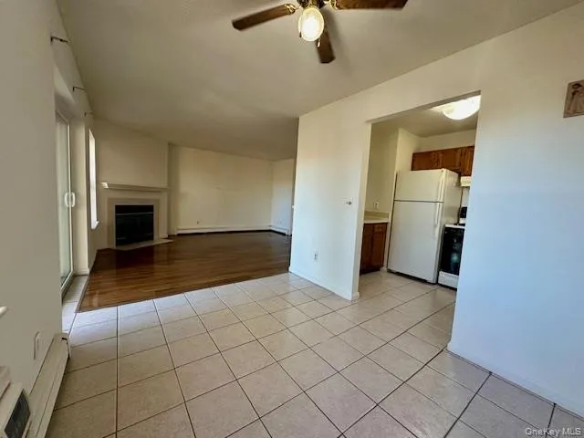Unfurnished living room featuring light tile patterned floors, baseboard heating, a fireplace with flush hearth, a ceiling fan, and a baseboard radiator Unfurnished living room featuring light tile patterned floors, baseboard heating, a fireplace with flush hearth, a ceiling fan, and a baseboard radiator