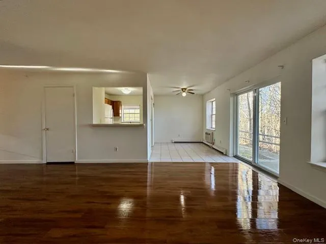 Unfurnished living room featuring wood finished floors, a wall mounted air conditioner, ceiling fan, and a baseboard heating unit Unfurnished living room featuring wood finished floors, a wall mounted air conditioner, ceiling fan, and a baseboard heating unit