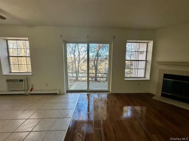 Unfurnished living room featuring plenty of natural light, a tiled fireplace, wood finished floors, and a baseboard radiator Unfurnished living room featuring plenty of natural light, a tiled fireplace, wood finished floors, and a baseboard radiator