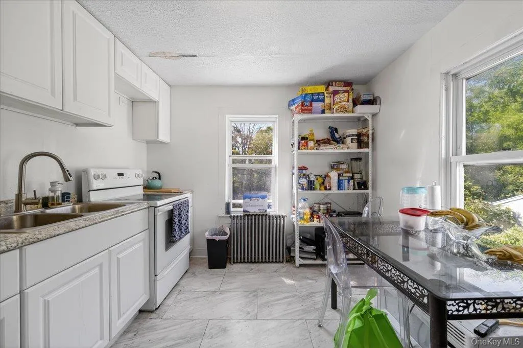 Kitchen featuring white cabinets, electric range, radiator heating unit, a textured ceiling, and light countertops Kitchen featuring white cabinets, electric range, radiator heating unit, a textured ceiling, and light countertops