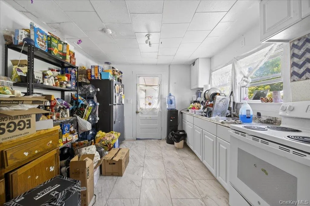 Kitchen featuring electric stove, freestanding refrigerator, light countertops, light marble finish flooring, and white cabinets Kitchen featuring electric stove, freestanding refrigerator, light countertops, light marble finish flooring, and white cabinets
