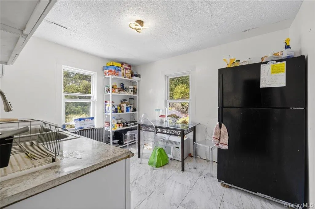 Kitchen with freestanding refrigerator, a textured ceiling, light marble finish floors, plenty of natural light, and light countertops Kitchen with freestanding refrigerator, a textured ceiling, light marble finish floors, plenty of natural light, and light countertops