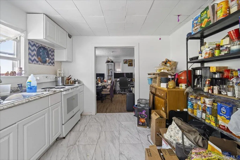 Kitchen featuring white cabinetry, white electric stove, a desk, light countertops, and light marble finish floors Kitchen featuring white cabinetry, white electric stove, a desk, light countertops, and light marble finish floors