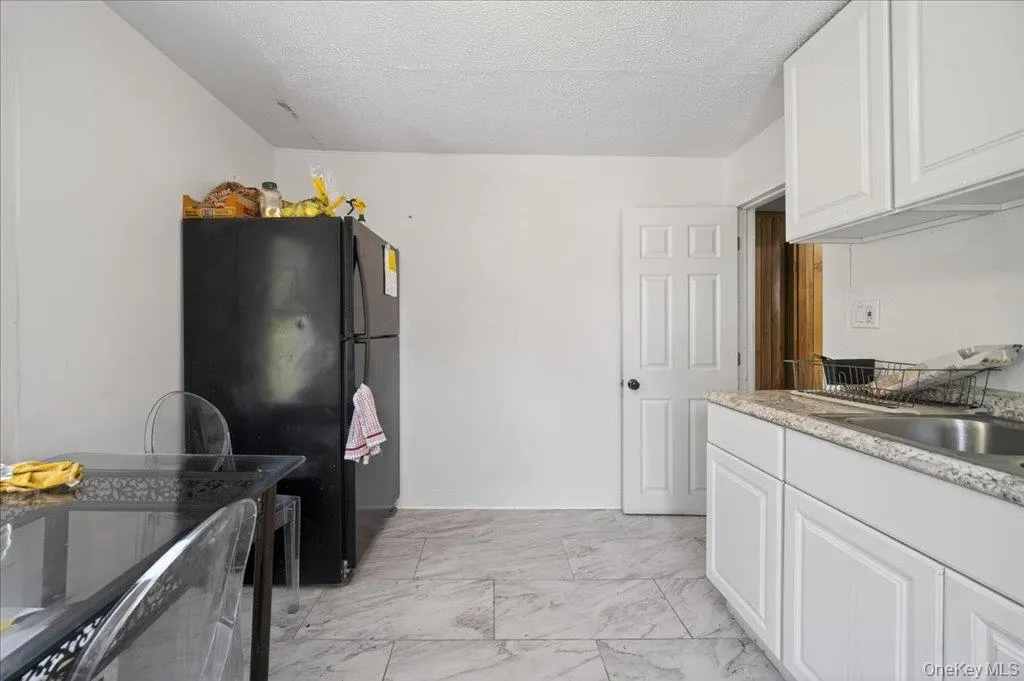Kitchen with white cabinetry, freestanding refrigerator, a textured ceiling, light marble finish flooring, and light stone countertops Kitchen with white cabinetry, freestanding refrigerator, a textured ceiling, light marble finish flooring, and light stone countertops