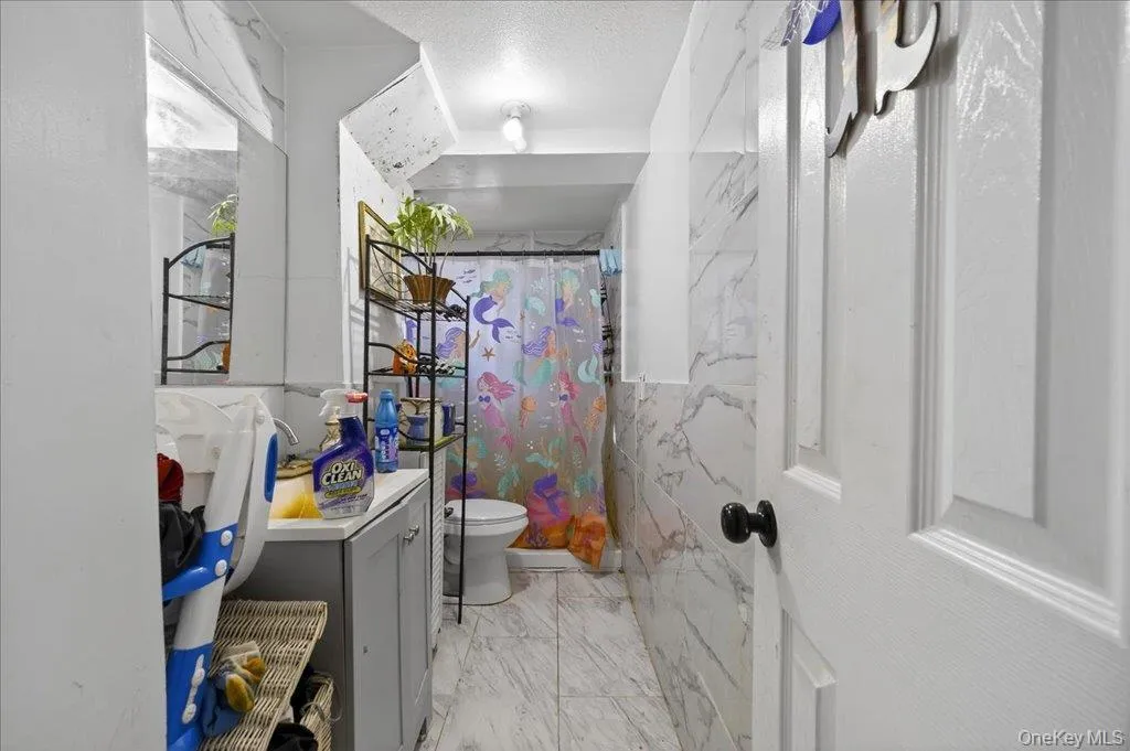 Full bathroom with tile walls, vanity, a shower with shower curtain, and light marble finish floors Full bathroom with tile walls, vanity, a shower with shower curtain, and light marble finish floors