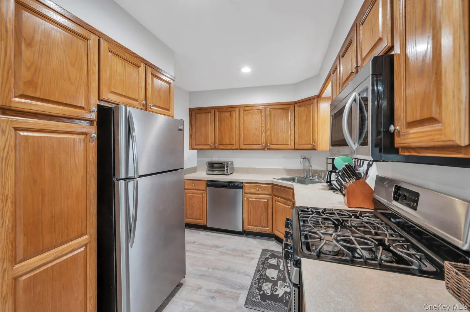 Kitchen with stainless steel appliances, light countertops, light wood-type flooring, brown cabinets, and recessed lighting Kitchen with stainless steel appliances, light countertops, light wood-type flooring, brown cabinets, and recessed lighting