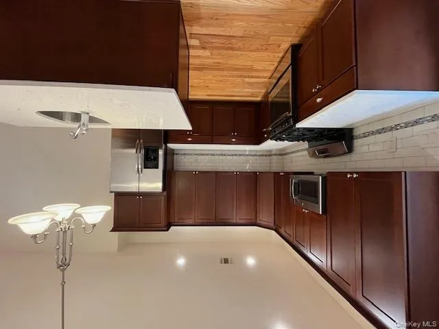 Kitchen featuring appliances with stainless steel finishes, hanging light fixtures, light stone countertops, decorative backsplash, and light wood-type flooring Kitchen featuring appliances with stainless steel finishes, hanging light fixtures, light stone countertops, decorative backsplash, and light wood-type flooring