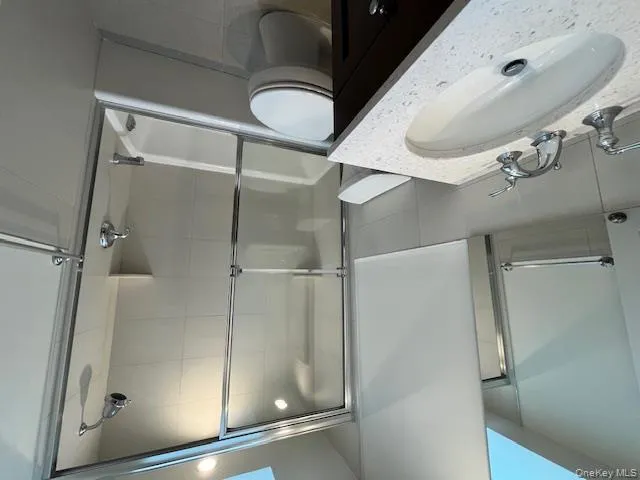 Bathroom with a skylight, shower / bath combination with glass door, vanity, tile walls, and tile patterned flooring Bathroom with a skylight, shower / bath combination with glass door, vanity, tile walls, and tile patterned flooring