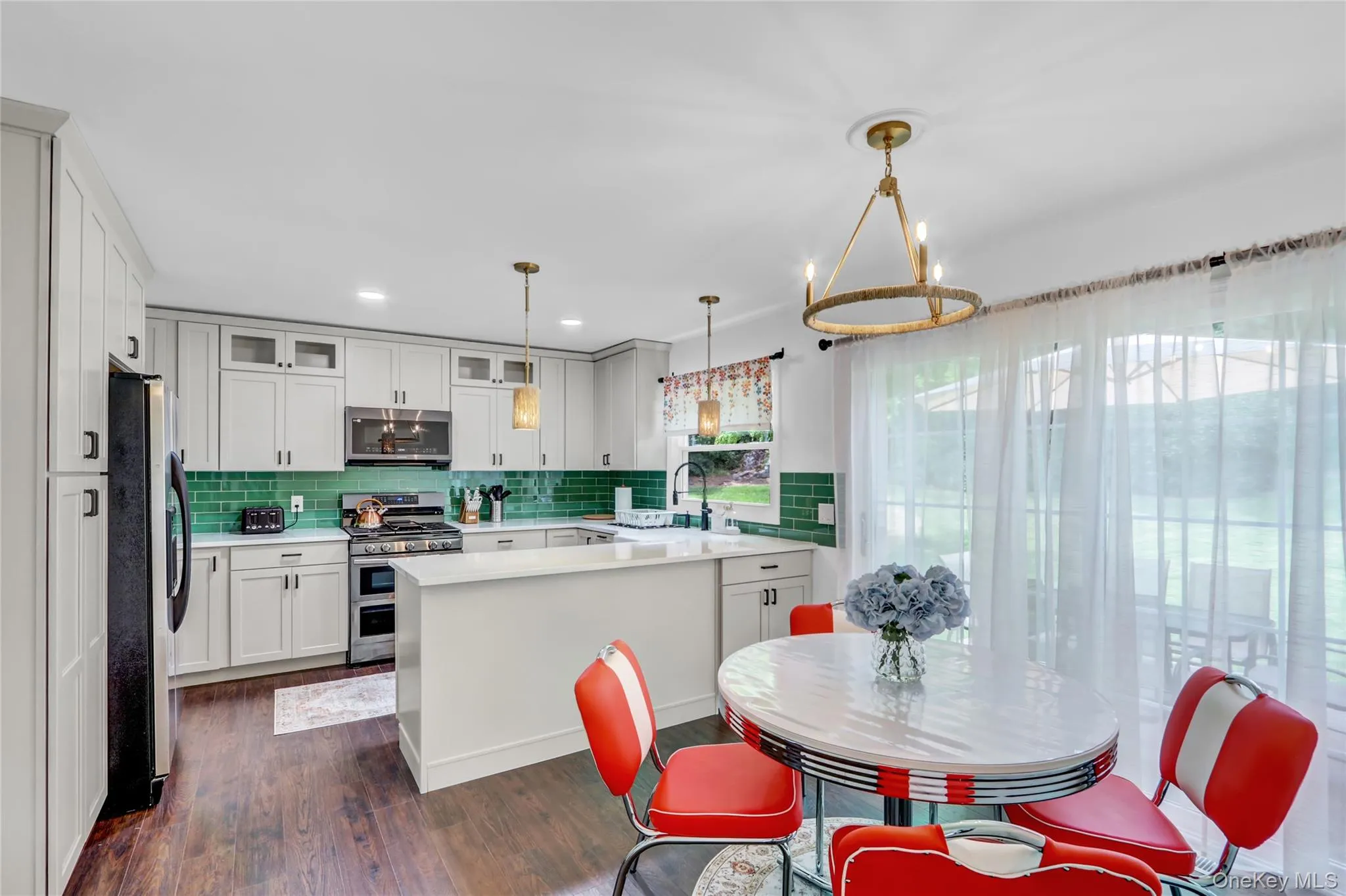 Kitchen with stainless steel appliances, glass insert cabinets, tasteful backsplash, dark wood finished floors, and a chandelier Kitchen with stainless steel appliances, glass insert cabinets, tasteful backsplash, dark wood finished floors, and a chandelier