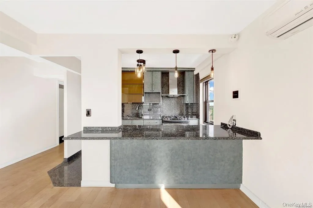 Kitchen featuring a peninsula, tasteful backsplash, a wall mounted AC, hanging light fixtures, and dark stone counters Kitchen featuring a peninsula, tasteful backsplash, a wall mounted AC, hanging light fixtures, and dark stone counters