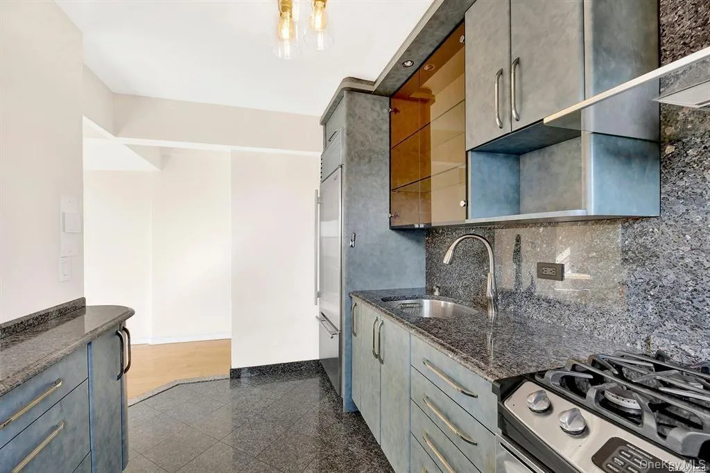 Kitchen featuring granite floors, stainless steel appliances, backsplash, open shelves, and dark stone countertops Kitchen featuring granite floors, stainless steel appliances, backsplash, open shelves, and dark stone countertops