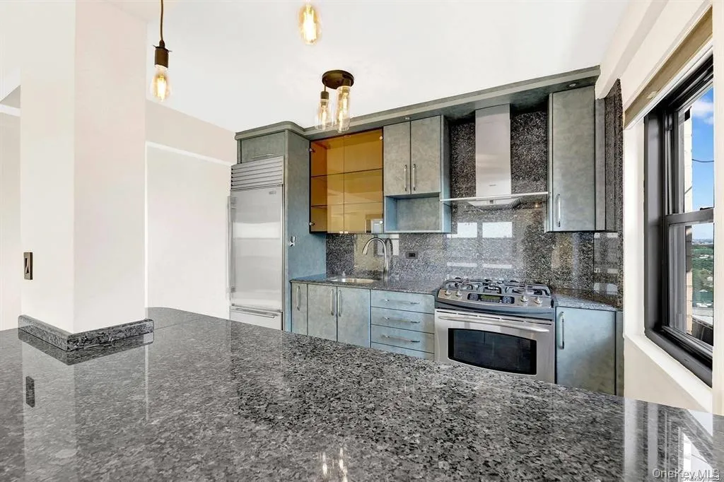 Kitchen with wall chimney range hood, stainless steel appliances, tasteful backsplash, and dark stone countertops Kitchen with wall chimney range hood, stainless steel appliances, tasteful backsplash, and dark stone countertops
