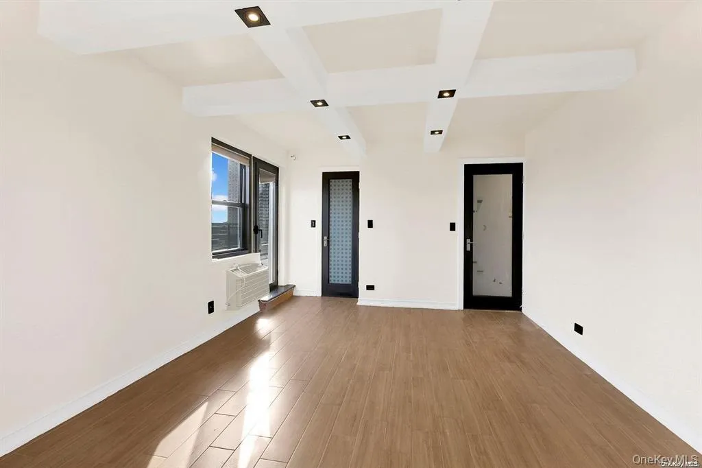 Empty room featuring coffered ceiling, beamed ceiling, light wood-style flooring, and a wall mounted air conditioner Empty room featuring coffered ceiling, beamed ceiling, light wood-style flooring, and a wall mounted air conditioner
