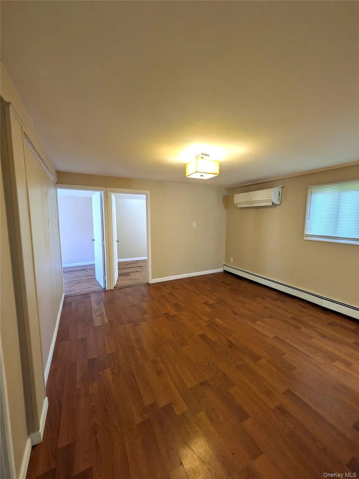 living room with dark wood-style flooring, a baseboard heating unit, and an AC wall unit living room with dark wood-style flooring, a baseboard heating unit, and an AC wall unit