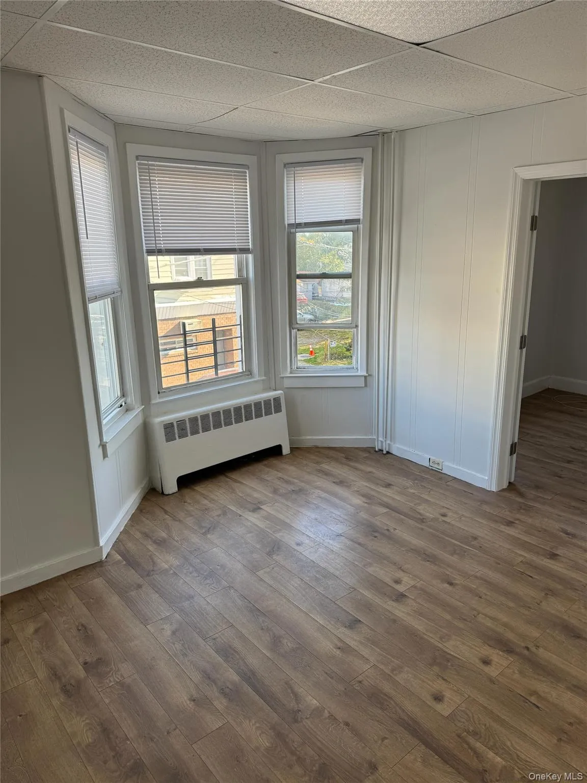 Unfurnished bedroom featuring radiator heating unit, wood finished floors, and a paneled ceiling Unfurnished bedroom featuring radiator heating unit, wood finished floors, and a paneled ceiling
