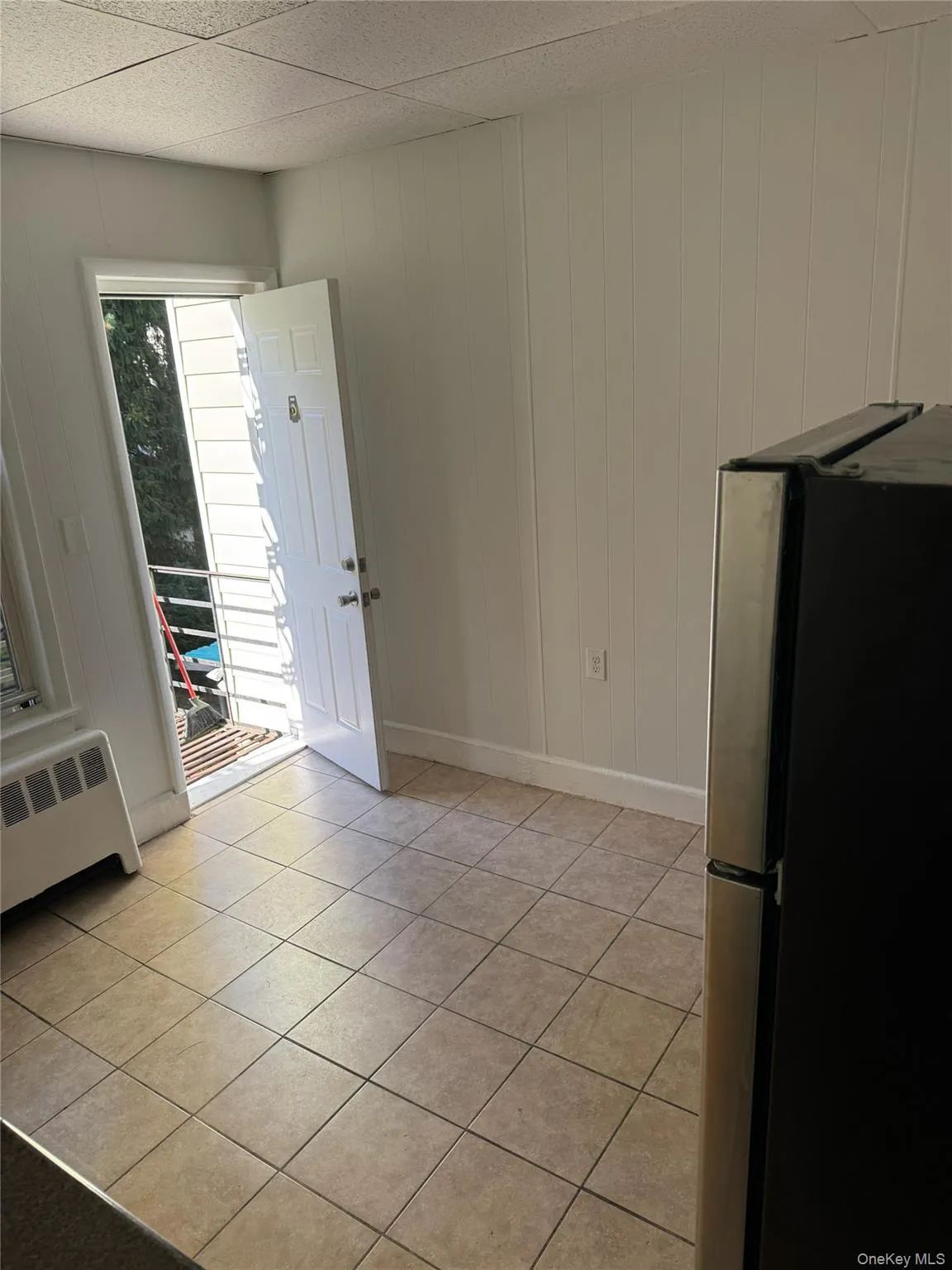 Unfurnished dining area featuring light tile patterned floors, radiator, and wood walls Unfurnished dining area featuring light tile patterned floors, radiator, and wood walls