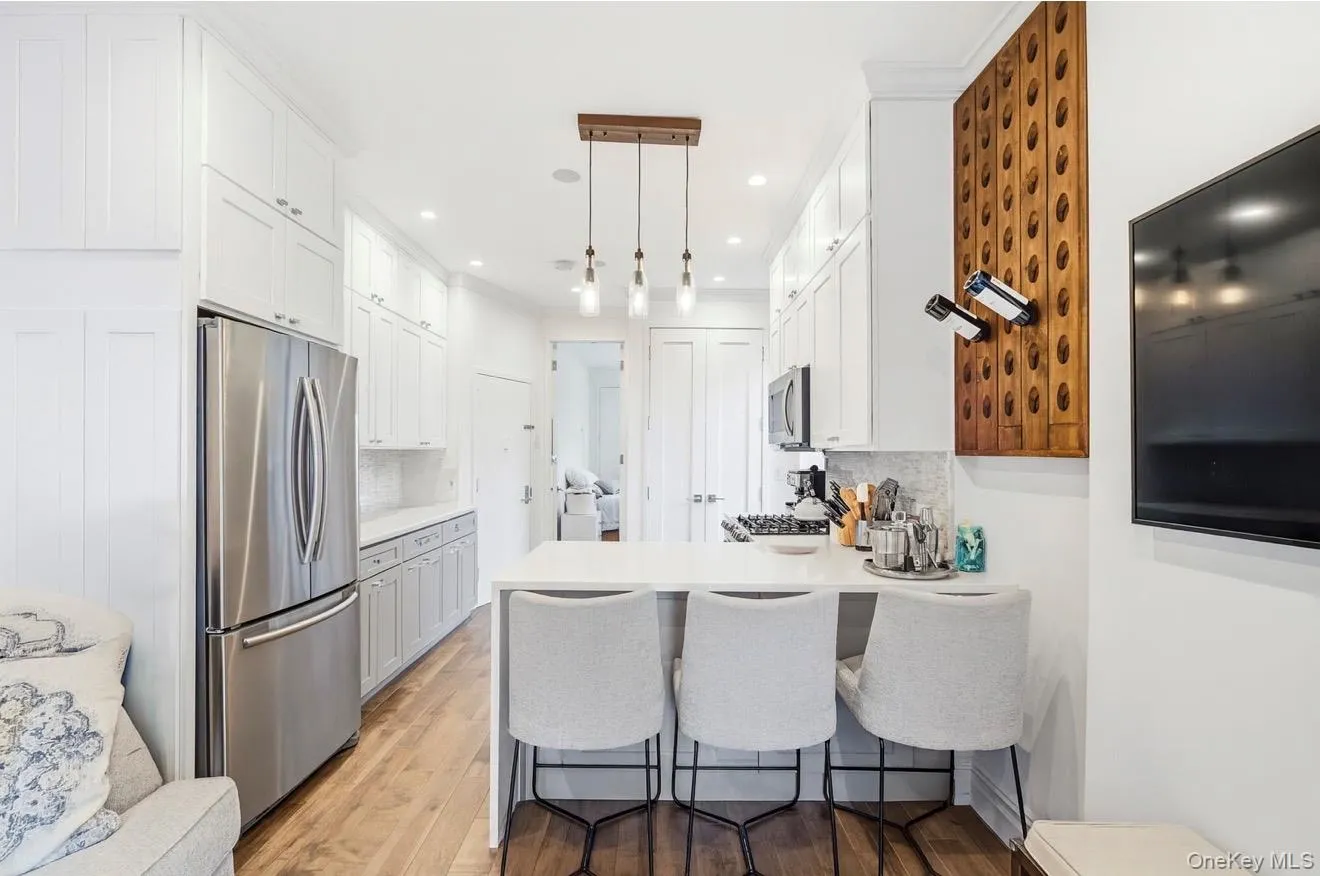 Kitchen with a kitchen bar, light wood finished floors, stainless steel appliances, a peninsula, and white cabinetry Kitchen with a kitchen bar, light wood finished floors, stainless steel appliances, a peninsula, and white cabinetry