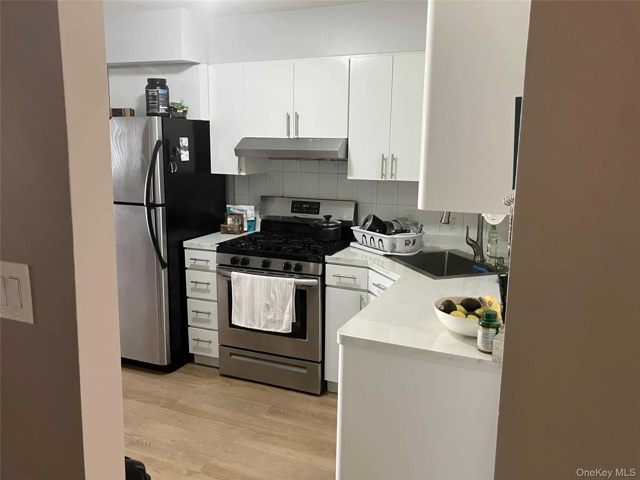 Kitchen with stainless steel appliances, tasteful backsplash, white cabinets, light wood-style floors, and under cabinet range hood Kitchen with stainless steel appliances, tasteful backsplash, white cabinets, light wood-style floors, and under cabinet range hood
