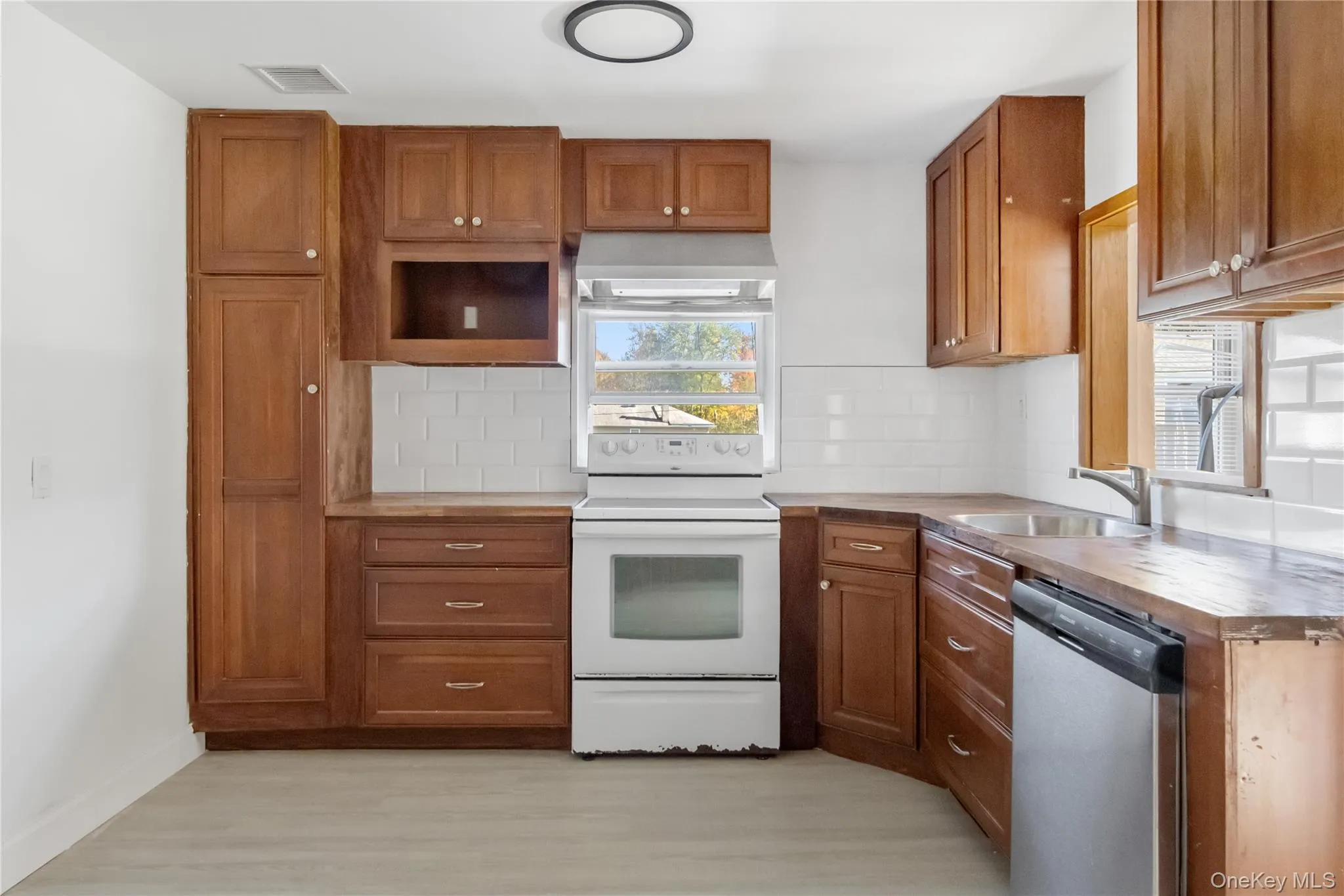 Kitchen featuring brown cabinets, white range with electric cooktop, ventilation hood, dishwasher, and wood counters Kitchen featuring brown cabinets, white range with electric cooktop, ventilation hood, dishwasher, and wood counters