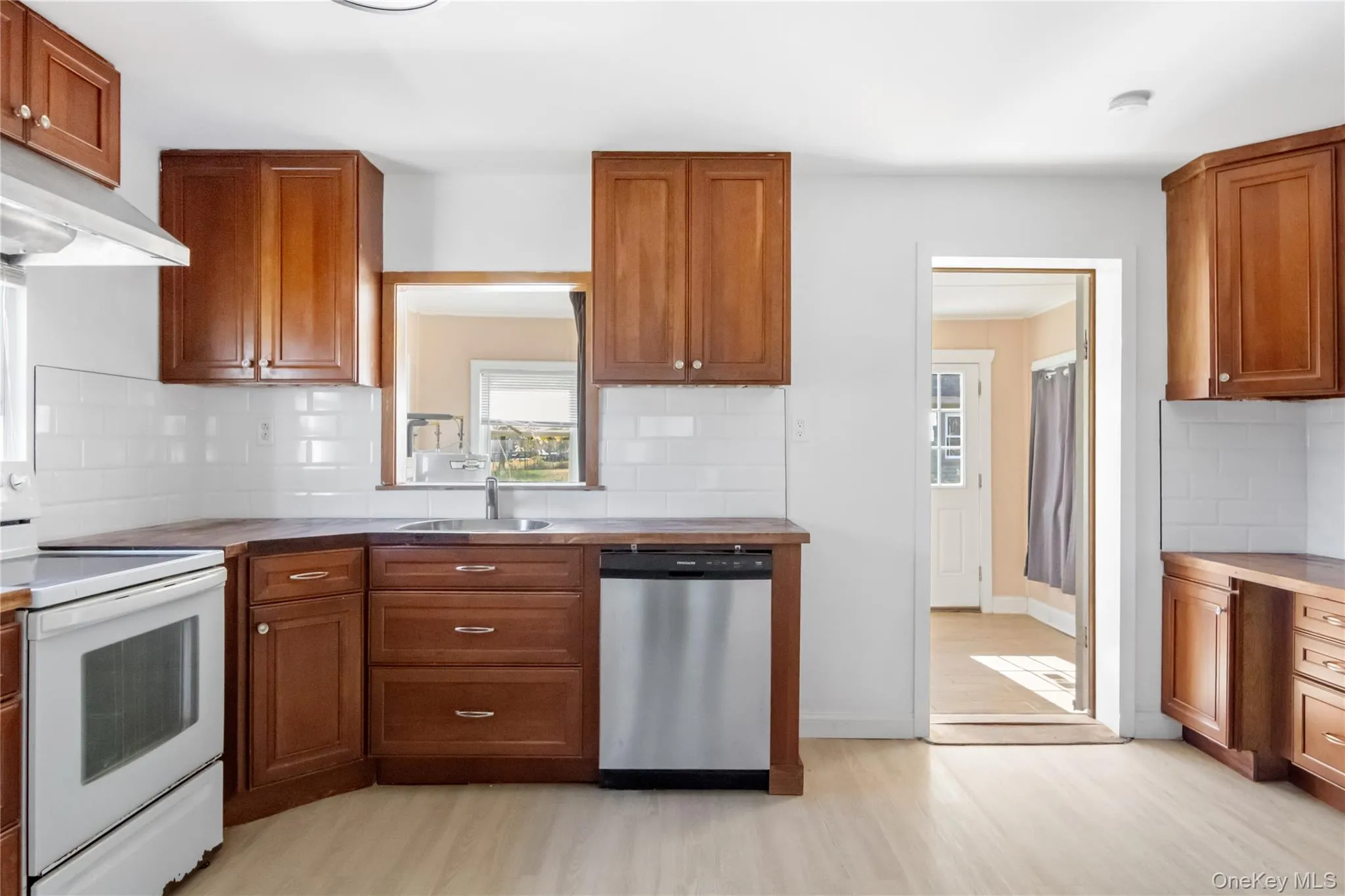 Kitchen featuring white electric range oven, backsplash, brown cabinetry, stainless steel dishwasher, and light wood-type flooring Kitchen featuring white electric range oven, backsplash, brown cabinetry, stainless steel dishwasher, and light wood-type flooring
