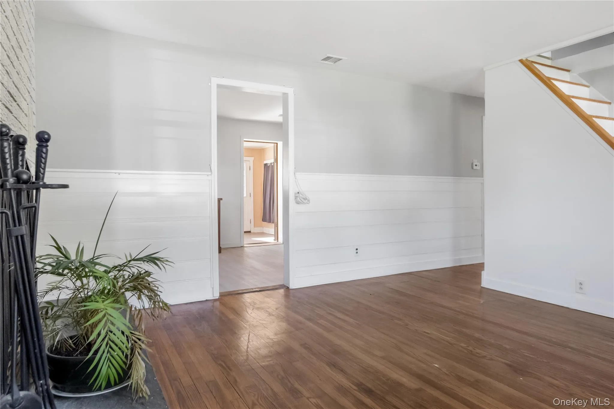 Empty room featuring dark wood-style flooring, a wainscoted wall, and stairway Empty room featuring dark wood-style flooring, a wainscoted wall, and stairway