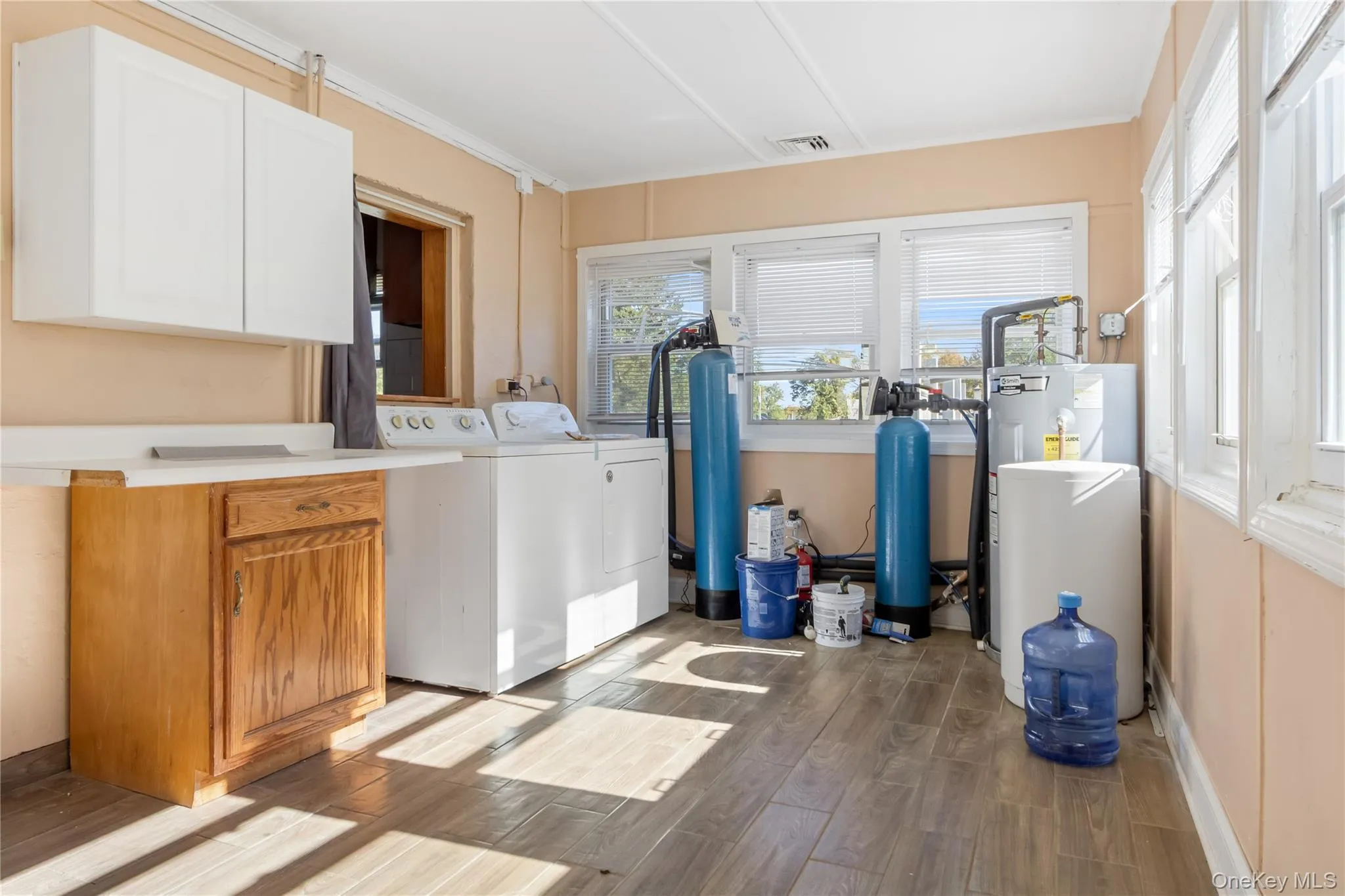 Laundry room with light wood finished floors, cabinet space, independent washer and dryer, crown molding, and electric water heater Laundry room with light wood finished floors, cabinet space, independent washer and dryer, crown molding, and electric water heater