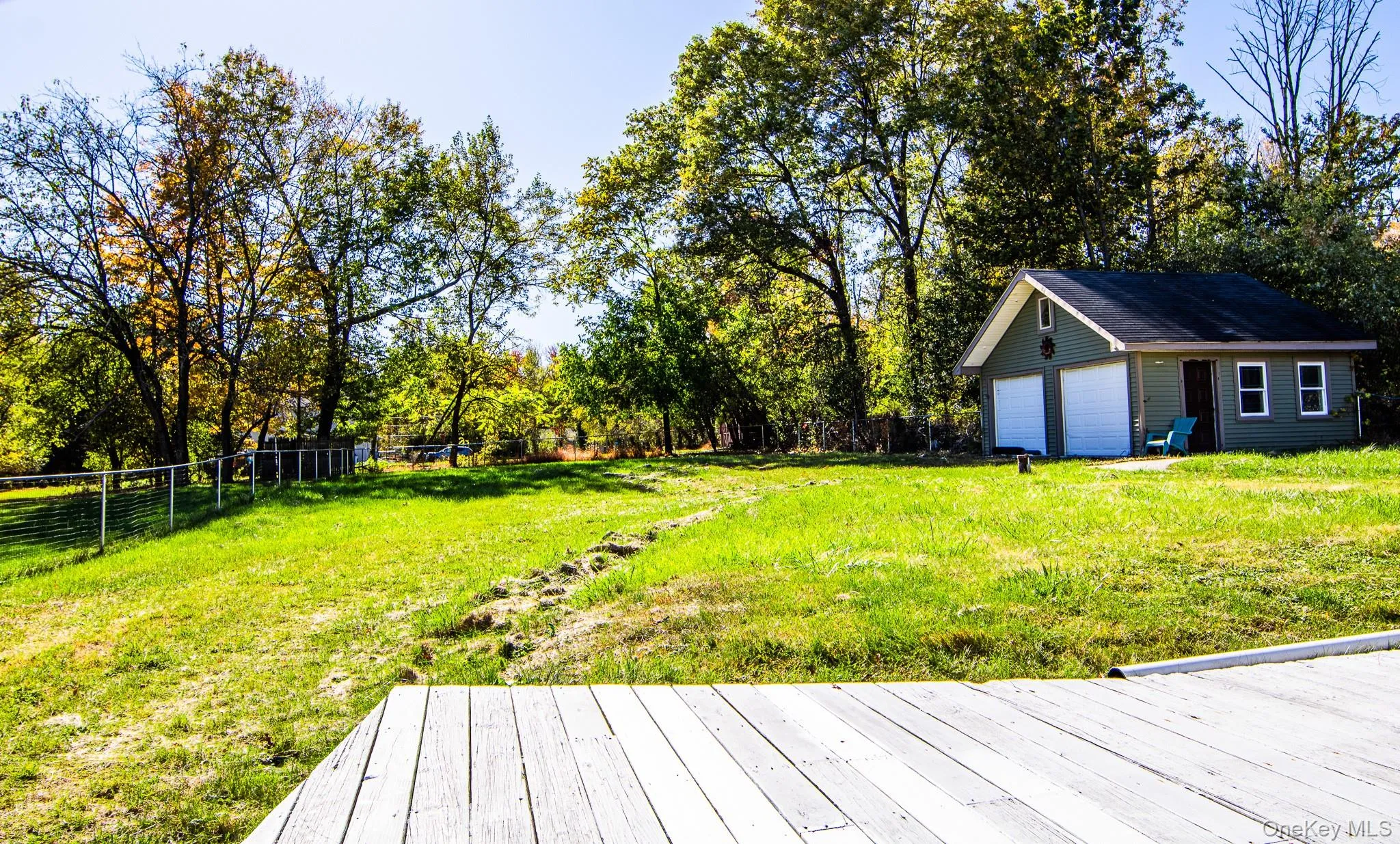 Fenced backyard with view of wooded area, a detached garage, and an outbuilding Fenced backyard with view of wooded area, a detached garage, and an outbuilding