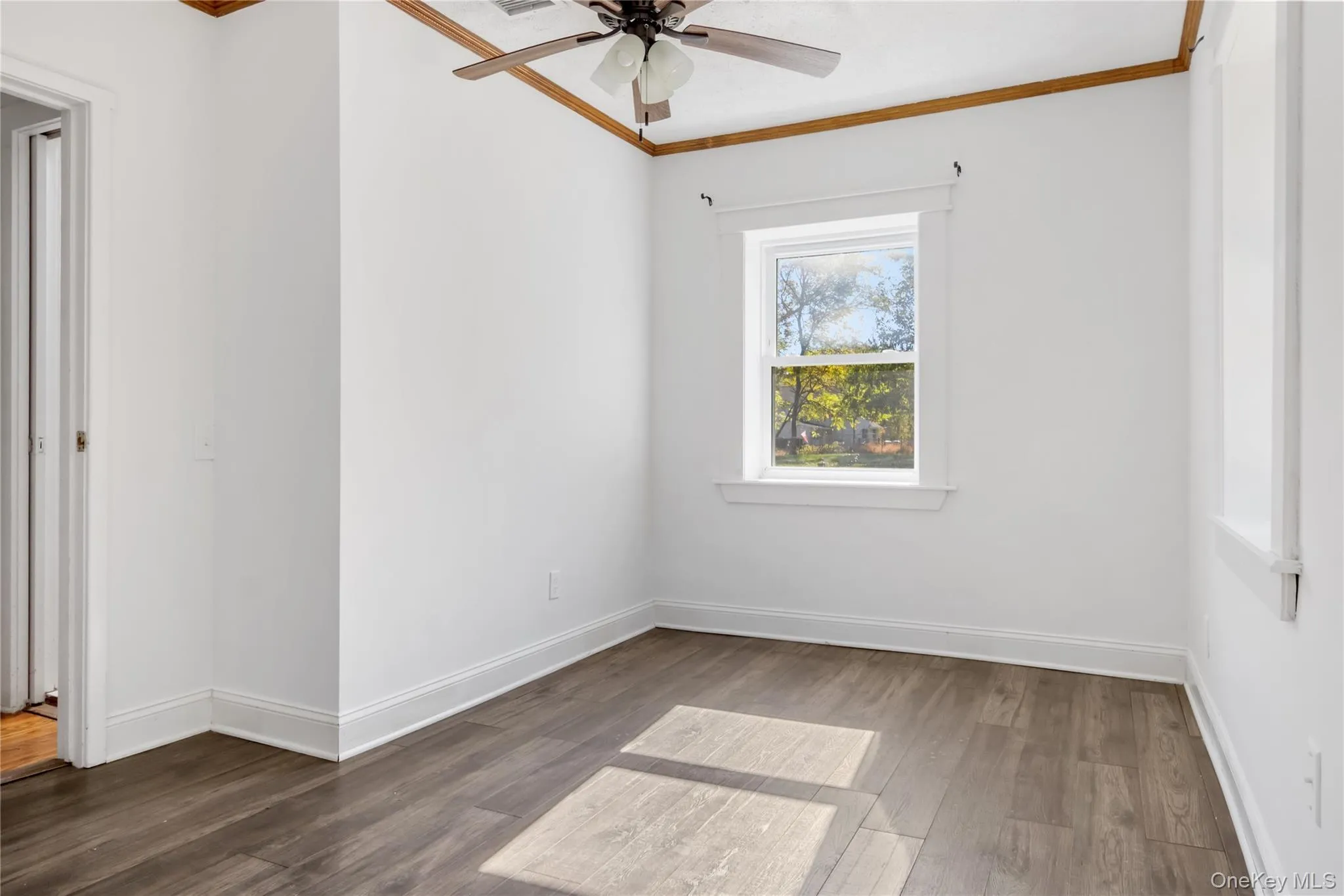 Unfurnished room featuring ornamental molding, dark wood-type flooring, and ceiling fan Unfurnished room featuring ornamental molding, dark wood-type flooring, and ceiling fan