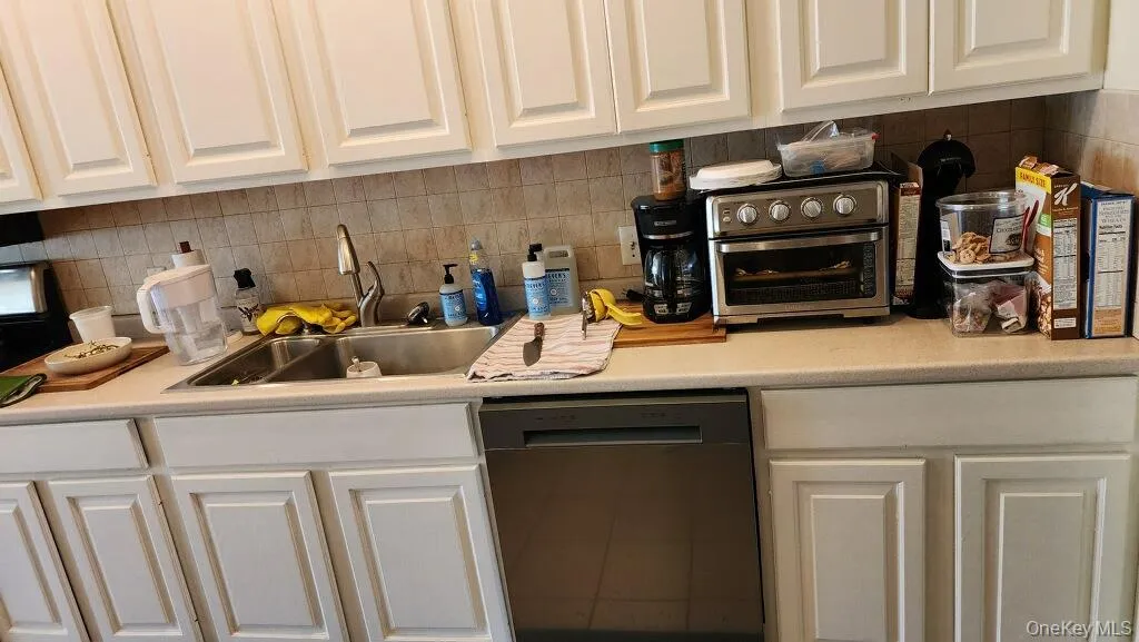 Kitchen with light countertops, dishwasher, decorative backsplash, and white cabinetry Kitchen with light countertops, dishwasher, decorative backsplash, and white cabinetry
