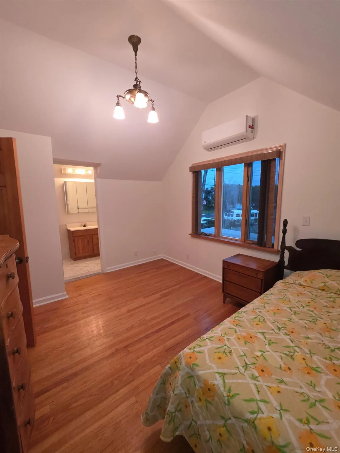 Bedroom with light wood-style flooring, vaulted ceiling, a chandelier, an AC wall unit, and connected bathroom Bedroom with light wood-style flooring, vaulted ceiling, a chandelier, an AC wall unit, and connected bathroom