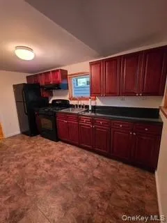 Kitchen with reddish brown cabinets, dark countertops, black appliances, and extractor fan Kitchen with reddish brown cabinets, dark countertops, black appliances, and extractor fan