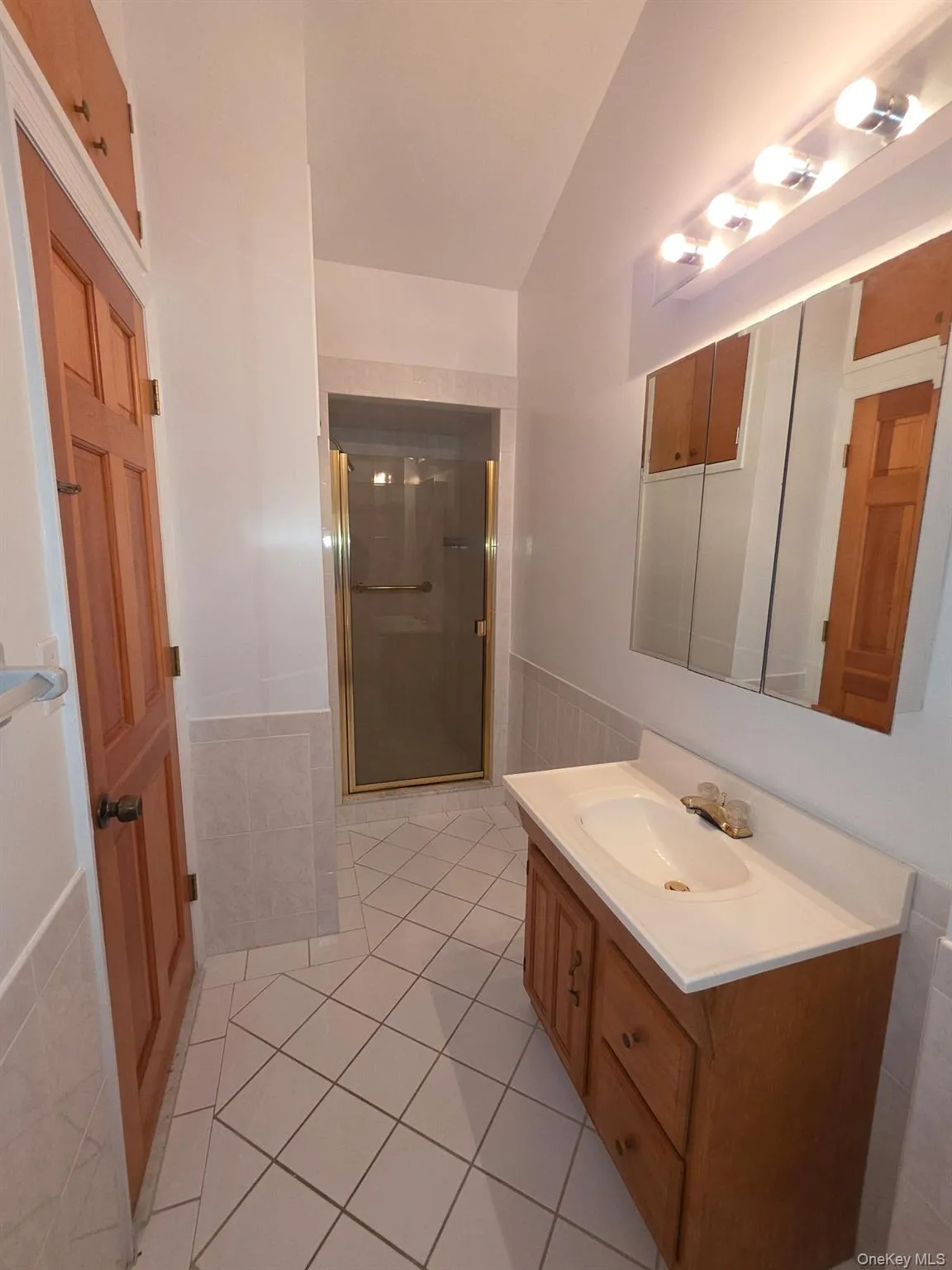 Bathroom with vanity, a shower stall, light tile patterned floors, wainscoting, and lofted ceiling Bathroom with vanity, a shower stall, light tile patterned floors, wainscoting, and lofted ceiling