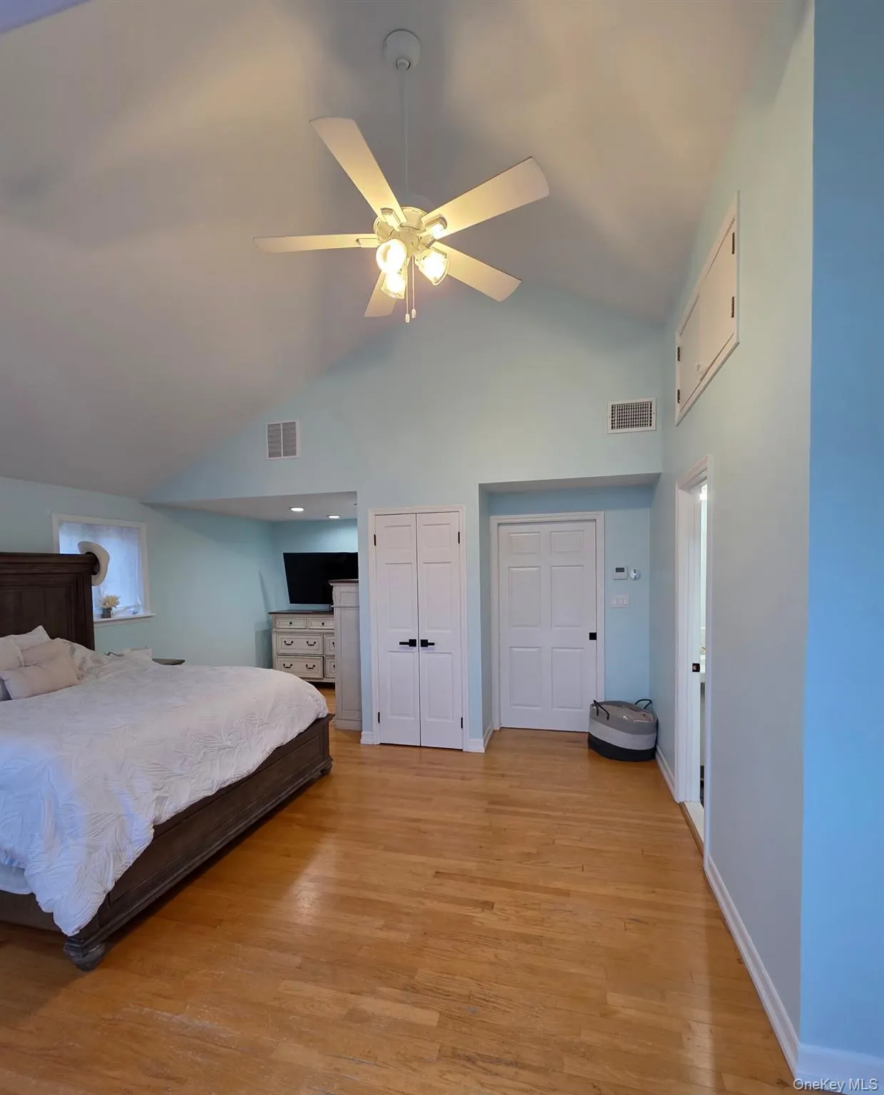 Bedroom with light wood-style flooring, high vaulted ceiling, two closets, and a ceiling fan Bedroom with light wood-style flooring, high vaulted ceiling, two closets, and a ceiling fan
