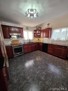 Kitchen with reddish brown cabinets, appliances with stainless steel finishes, plenty of natural light, and backsplash Kitchen with reddish brown cabinets, appliances with stainless steel finishes, plenty of natural light, and backsplash
