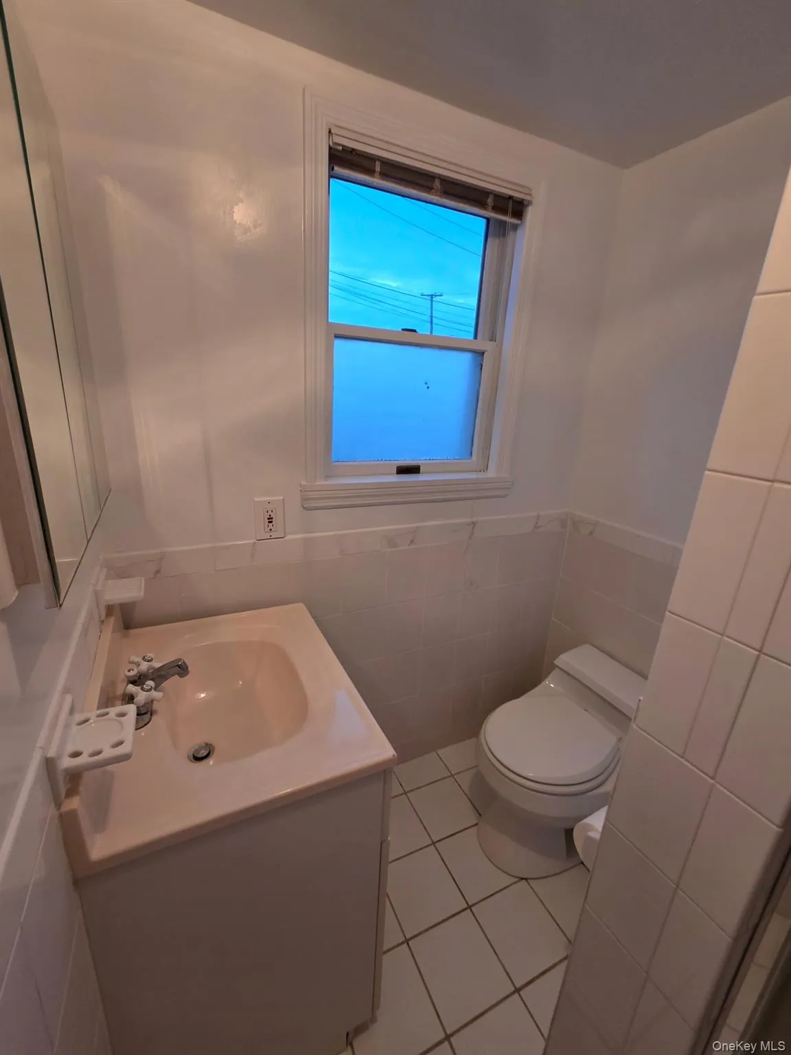 Half bath with vanity, light tile patterned floors, tile walls, and a wainscoted wall Half bath with vanity, light tile patterned floors, tile walls, and a wainscoted wall