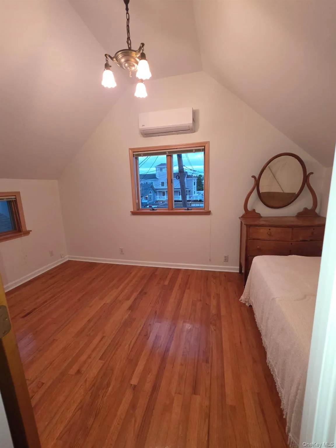 Unfurnished bedroom with light wood-style floors, lofted ceiling, a wall mounted AC, and a chandelier Unfurnished bedroom with light wood-style floors, lofted ceiling, a wall mounted AC, and a chandelier