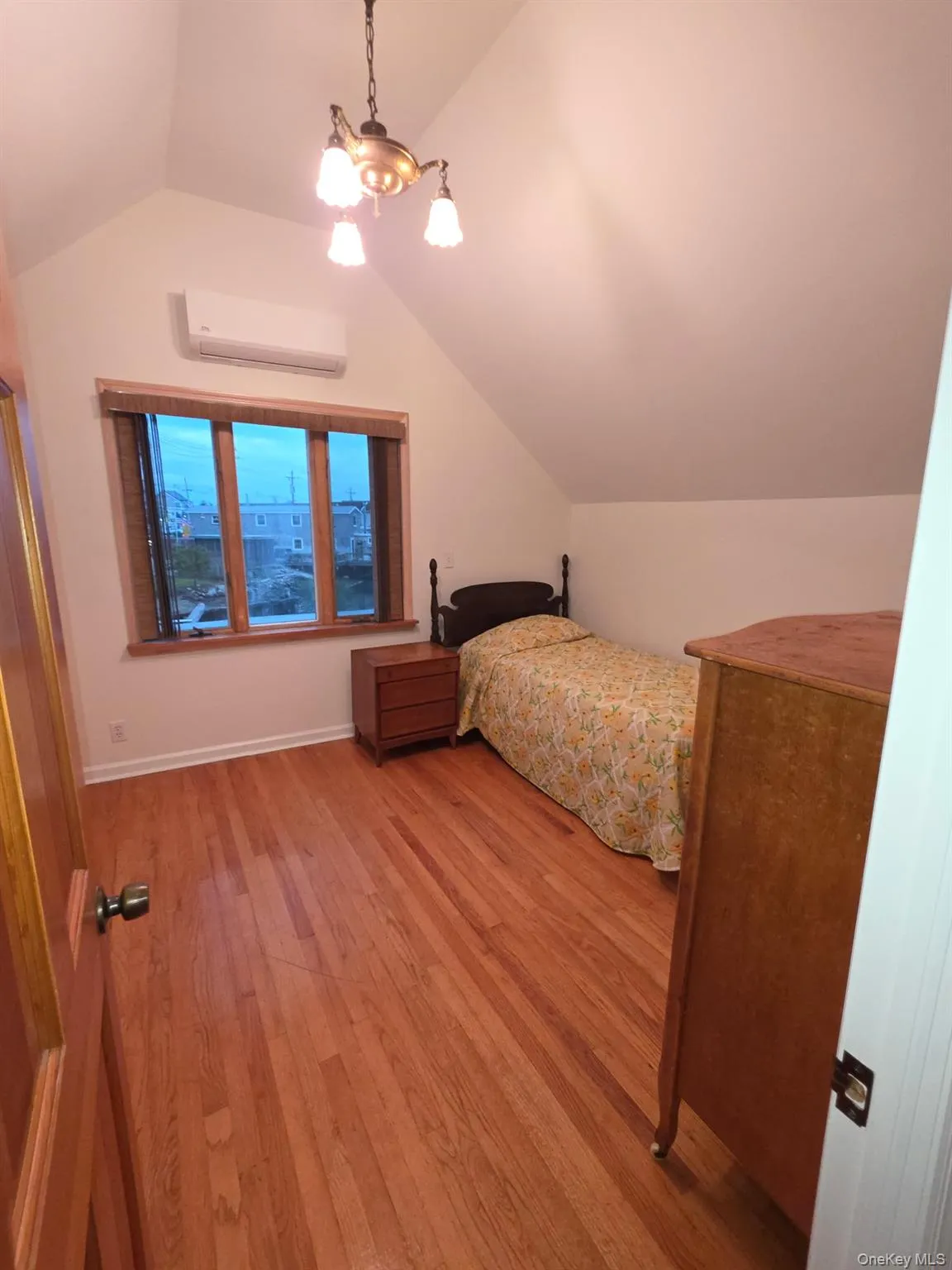 Bedroom featuring lofted ceiling, light wood-style floors, a wall mounted AC, and a chandelier Bedroom featuring lofted ceiling, light wood-style floors, a wall mounted AC, and a chandelier