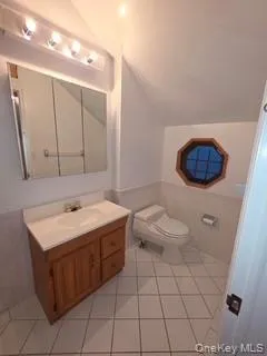Bathroom featuring lofted ceiling, vanity, light tile patterned floors, and wainscoting Bathroom featuring lofted ceiling, vanity, light tile patterned floors, and wainscoting