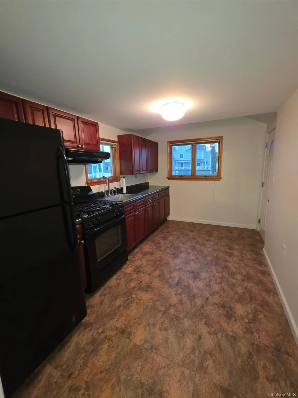 Kitchen featuring black appliances, dark countertops, under cabinet range hood, dark brown cabinets, and stone finish flooring Kitchen featuring black appliances, dark countertops, under cabinet range hood, dark brown cabinets, and stone finish flooring