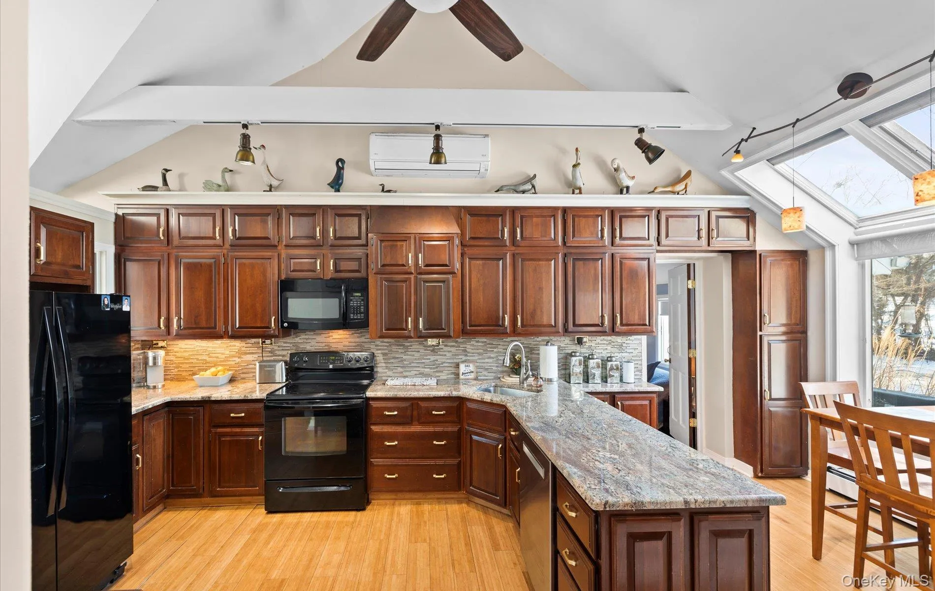 Kitchen featuring black appliances, light stone countertops, light wood-style flooring, vaulted ceiling, and a wall mounted AC Kitchen featuring black appliances, light stone countertops, light wood-style flooring, vaulted ceiling, and a wall mounted AC