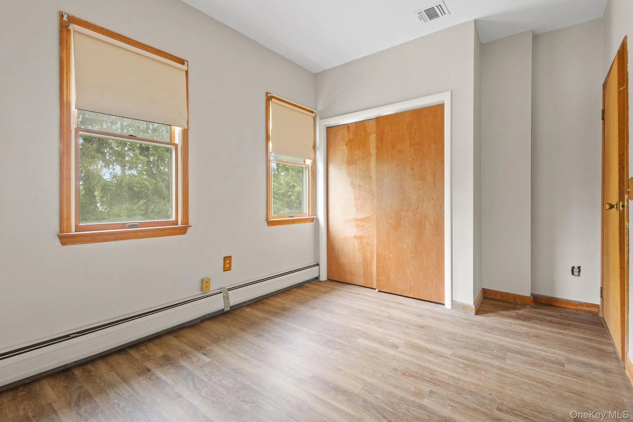 Unfurnished bedroom featuring baseboard heating, light wood-style flooring, baseboards, and a closet Unfurnished bedroom featuring baseboard heating, light wood-style flooring, baseboards, and a closet