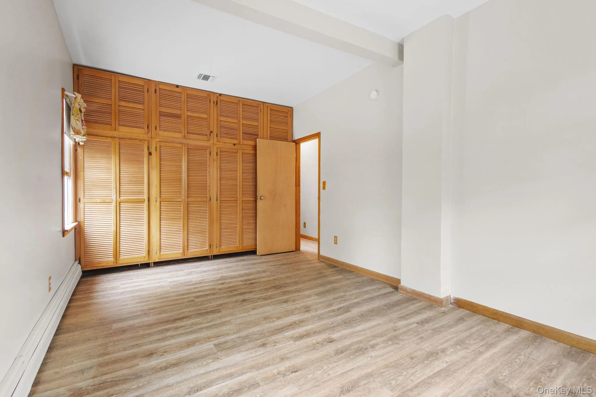 Unfurnished bedroom featuring a baseboard radiator, light wood finished floors, baseboards, and a closet Unfurnished bedroom featuring a baseboard radiator, light wood finished floors, baseboards, and a closet