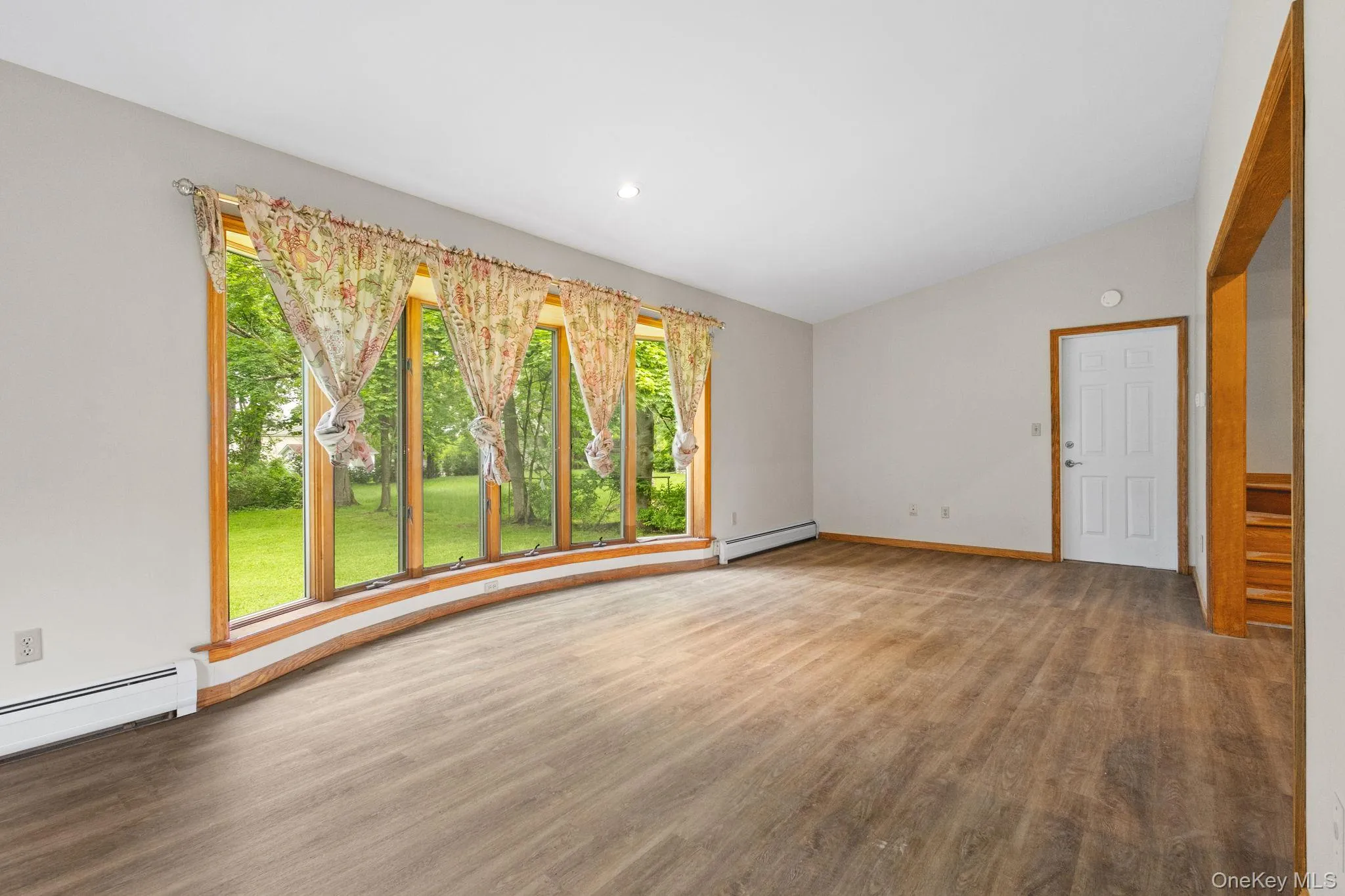 Spare room featuring a baseboard heating unit, healthy amount of natural light, wood finished floors, baseboards, and lofted ceiling Spare room featuring a baseboard heating unit, healthy amount of natural light, wood finished floors, baseboards, and lofted ceiling