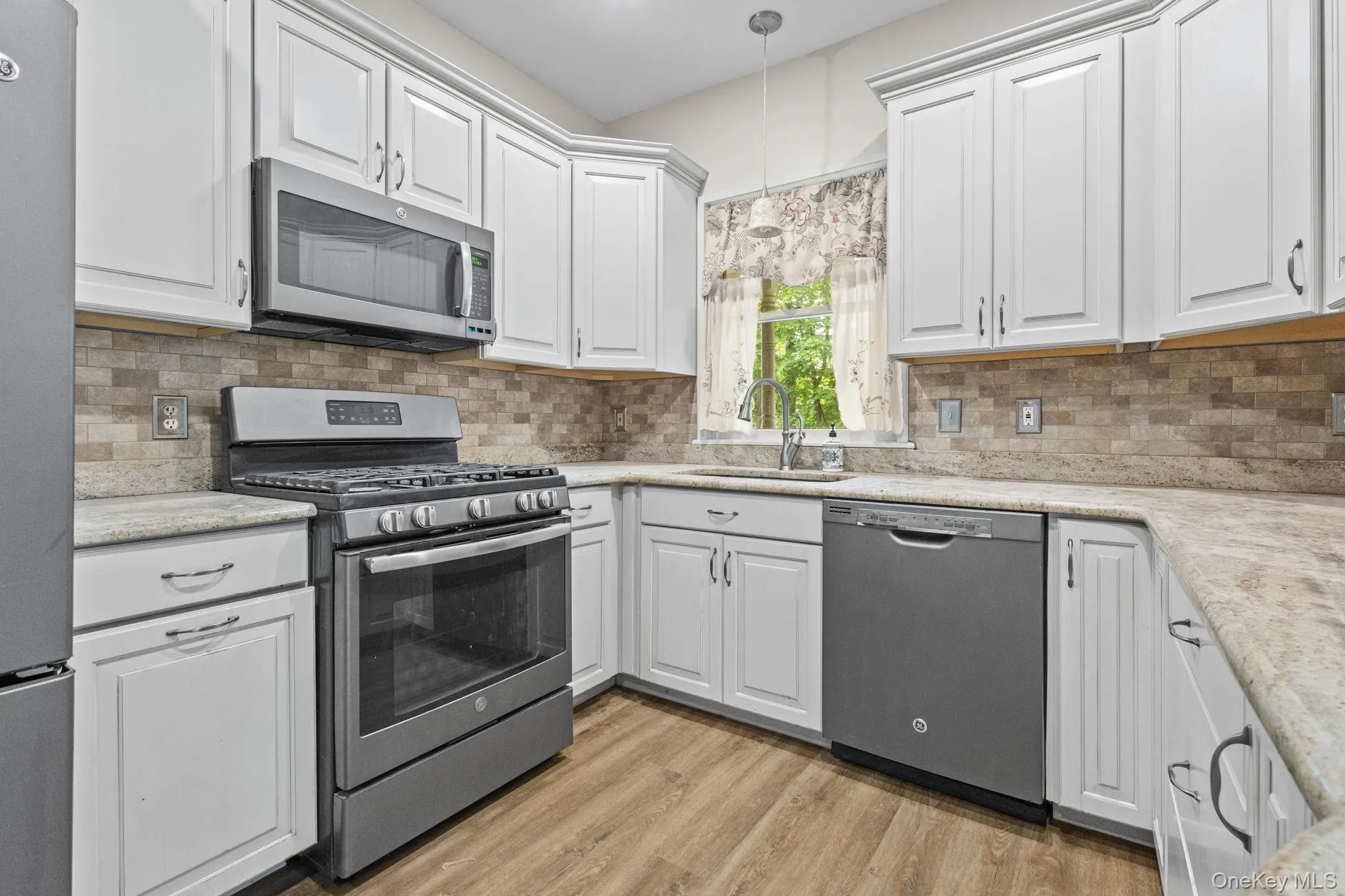 Kitchen with stainless steel appliances, a sink, white cabinetry, and light wood-style flooring Kitchen with stainless steel appliances, a sink, white cabinetry, and light wood-style flooring