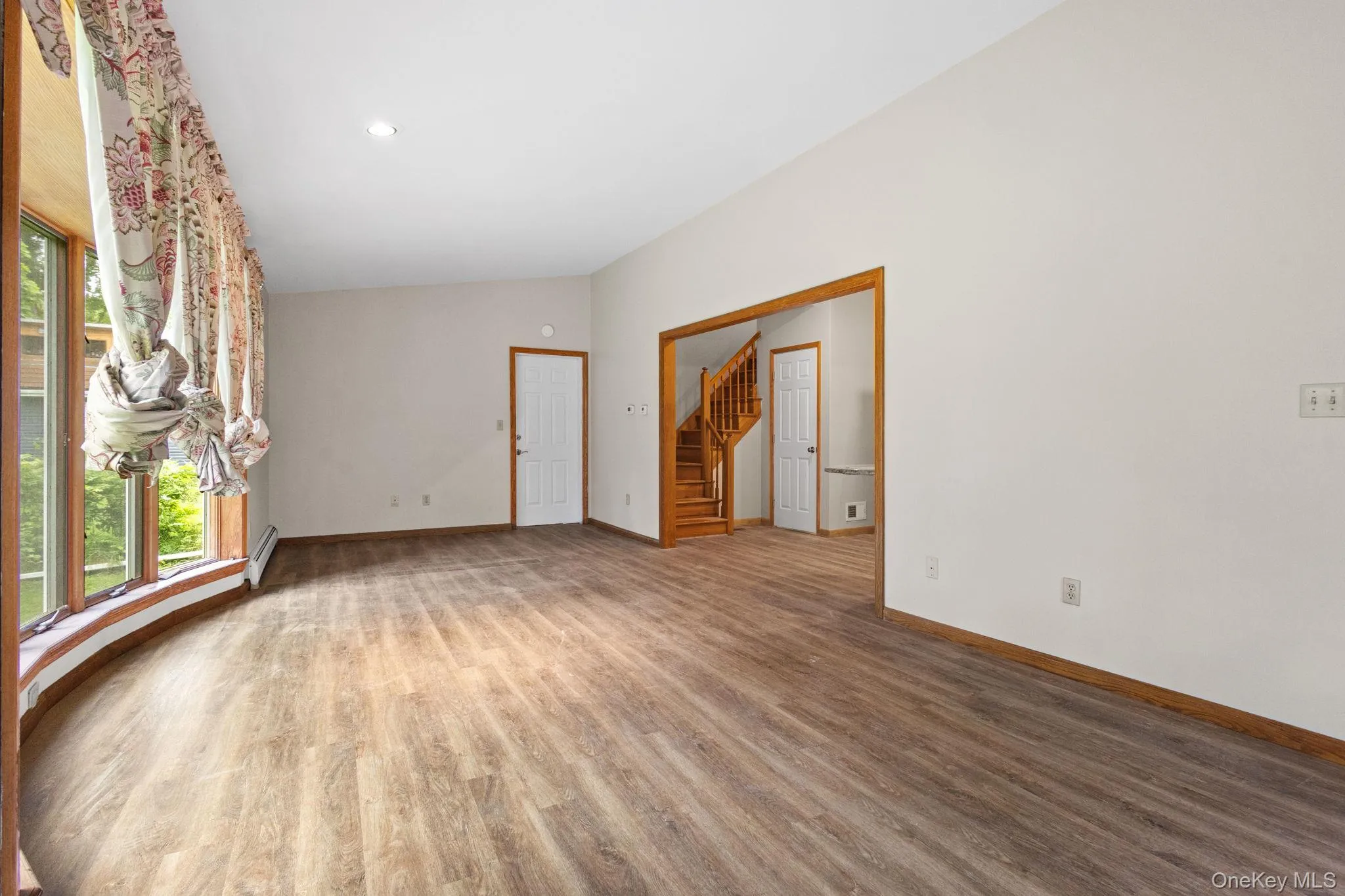 Empty room featuring wood finished floors, baseboards, baseboard heating, stairs, and recessed lighting Empty room featuring wood finished floors, baseboards, baseboard heating, stairs, and recessed lighting