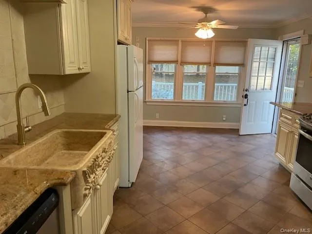 Kitchen with light stone counters, crown molding, appliances with stainless steel finishes, a ceiling fan, and tasteful backsplash Kitchen with light stone counters, crown molding, appliances with stainless steel finishes, a ceiling fan, and tasteful backsplash