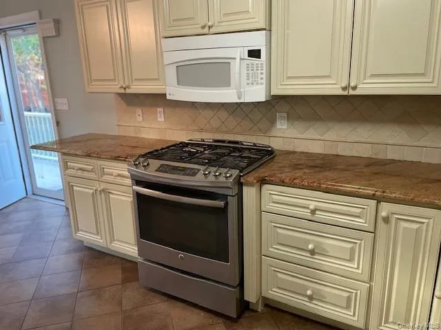 Kitchen featuring stainless steel gas range, white microwave, tasteful backsplash, and dark tile patterned flooring Kitchen featuring stainless steel gas range, white microwave, tasteful backsplash, and dark tile patterned flooring