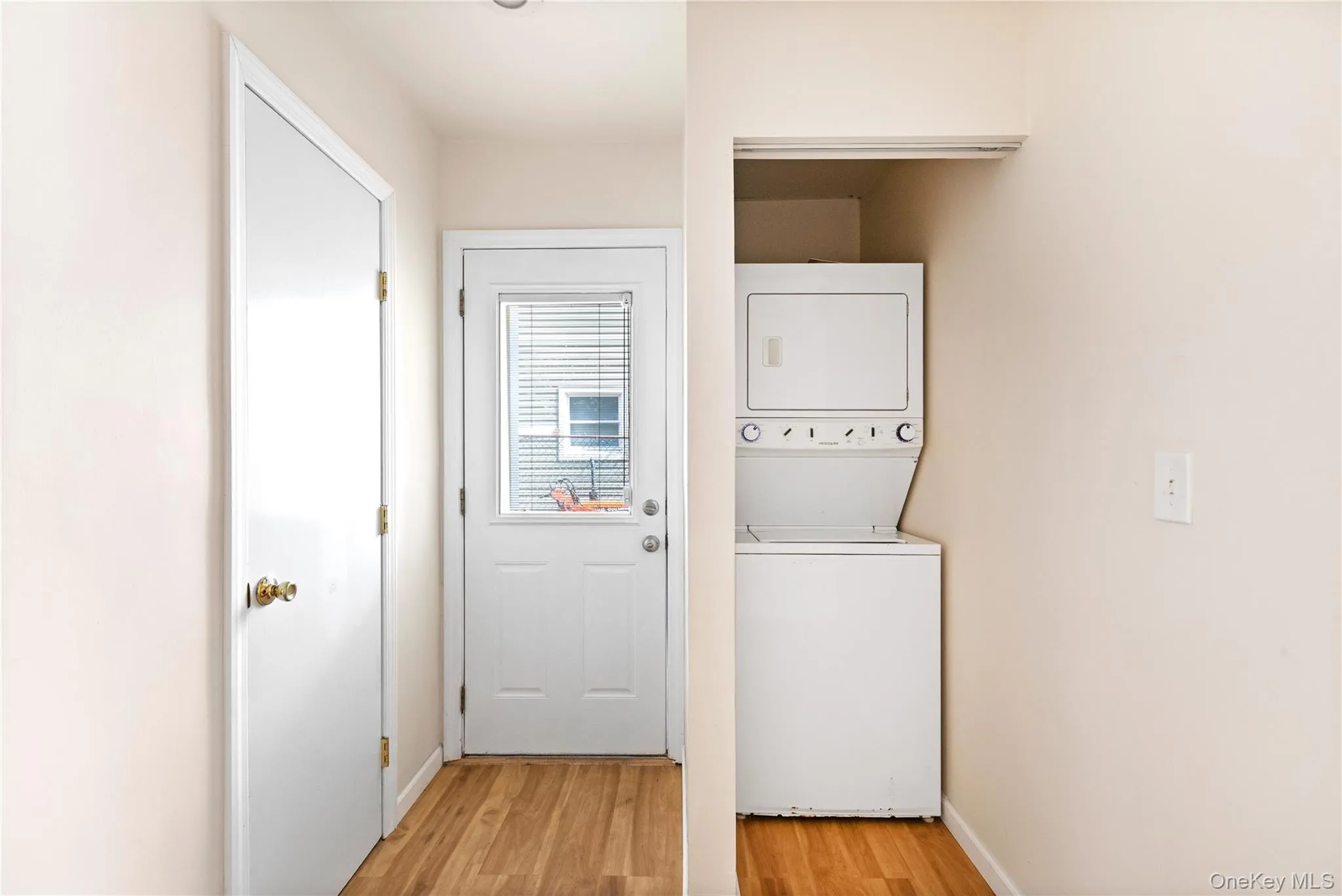 Washroom with light wood-type flooring and stacked washing machine and dryer Washroom with light wood-type flooring and stacked washing machine and dryer